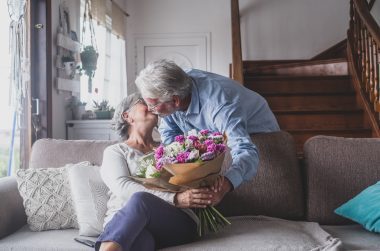 Grey-haired man giving flowers to his spouse.