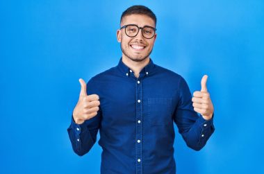 Hispanic man excited wearing a blue shirt with two thumbs up smiling.