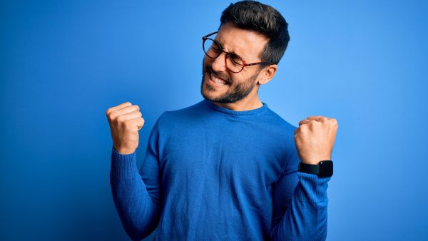 Man in glasses wearing blue sweater pumping his fists in excitement.